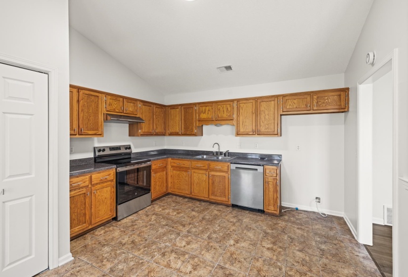 Kitchen featuring a vaulted ceiling, wood cabinetry, dark countertops, stainless steel appliances, and patterned tile flooring
