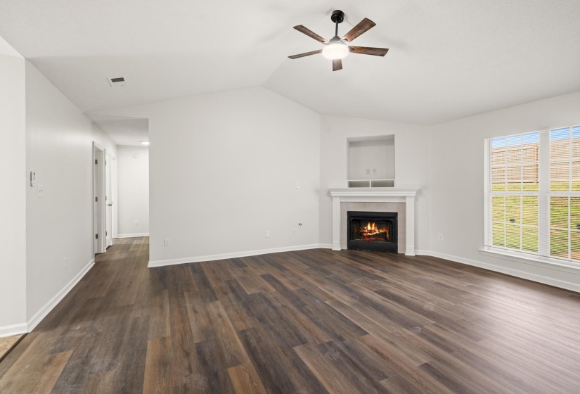 Spacious living area featuring wood-finish flooring, a fireplace with a white mantel, and an integrated ceiling fan