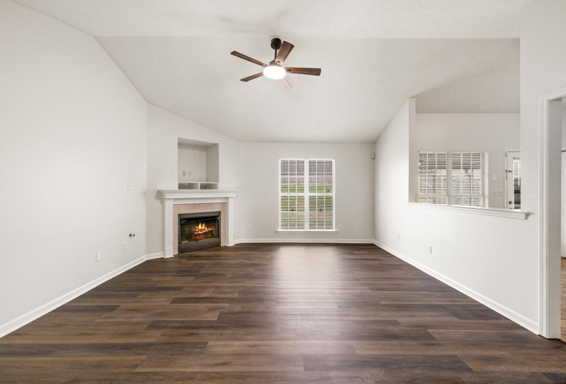 Spacious living area featuring wood-finish flooring, a vaulted ceiling, and a ceiling fan