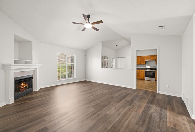 Spacious living area featuring wood-finish flooring, a white mantel fireplace, a ceiling fan with integrated lighting, and vaulted ceilings