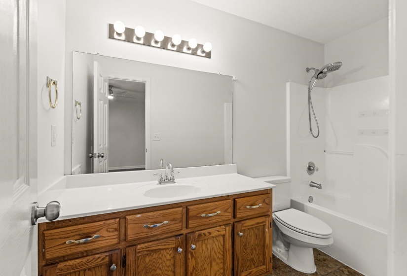 Bathroom featuring a wood-finish vanity with a white countertop and integrated sink, a large wall-mounted mirror, and overhead vanity lighting