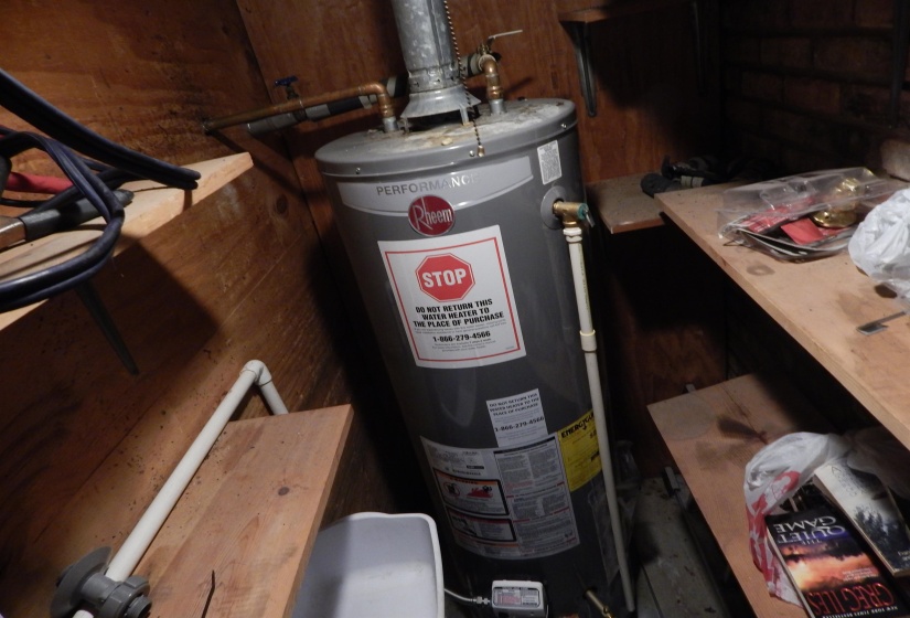 Water heater installation with exposed plumbing and wood-paneled walls