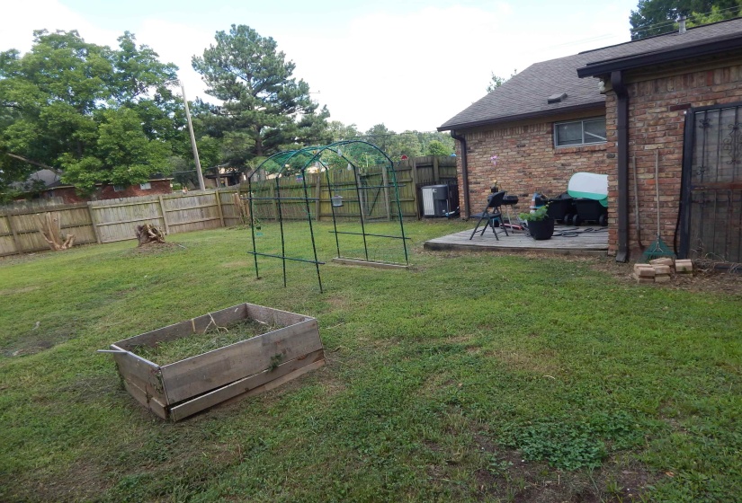 Expansive backyard featuring a wood privacy fence, a raised garden bed, and a brick exterior with a patio area