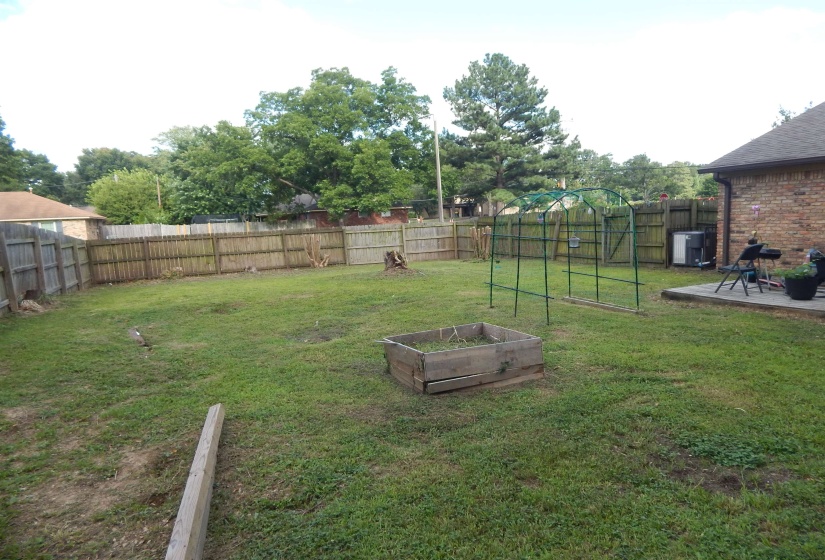 Spacious backyard featuring a wood privacy fence, concrete patio, and mature trees beyond the fence line