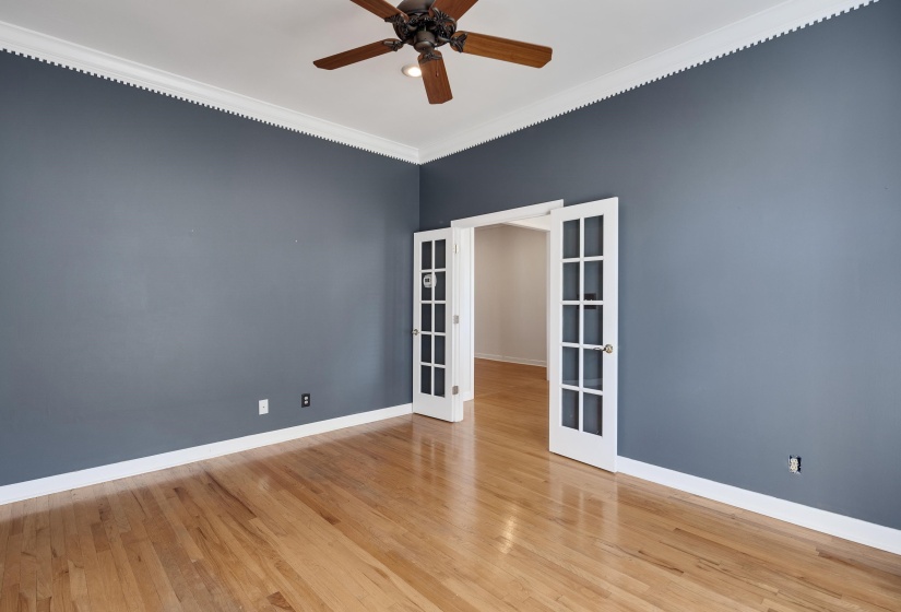 Expansive room featuring rich wood-finish flooring, a ceiling fan, and decorative crown molding