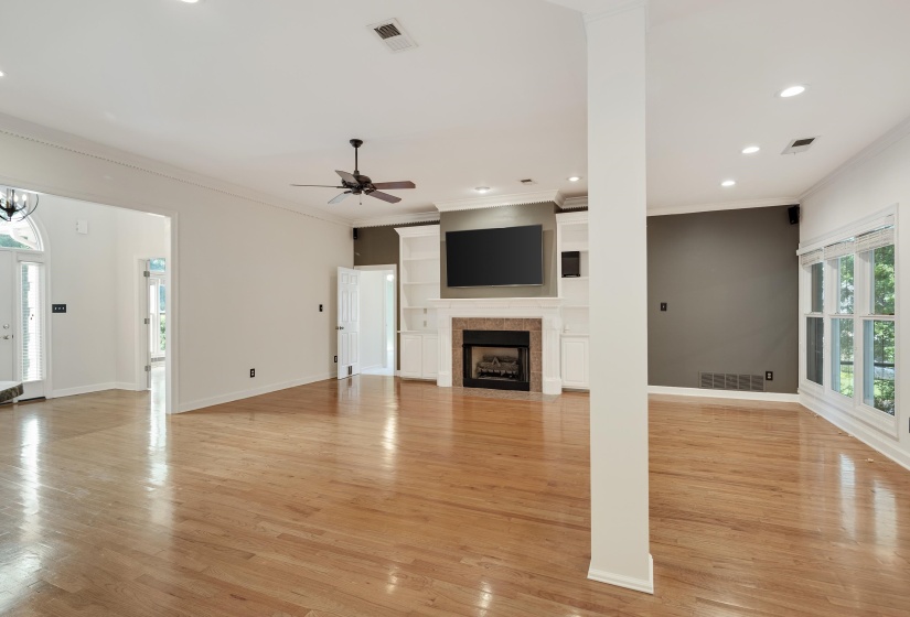 Spacious room featuring light wood-finish flooring, a fireplace with a stone surround and white mantel, built-in shelving, a ceiling fan, and recessed lighting