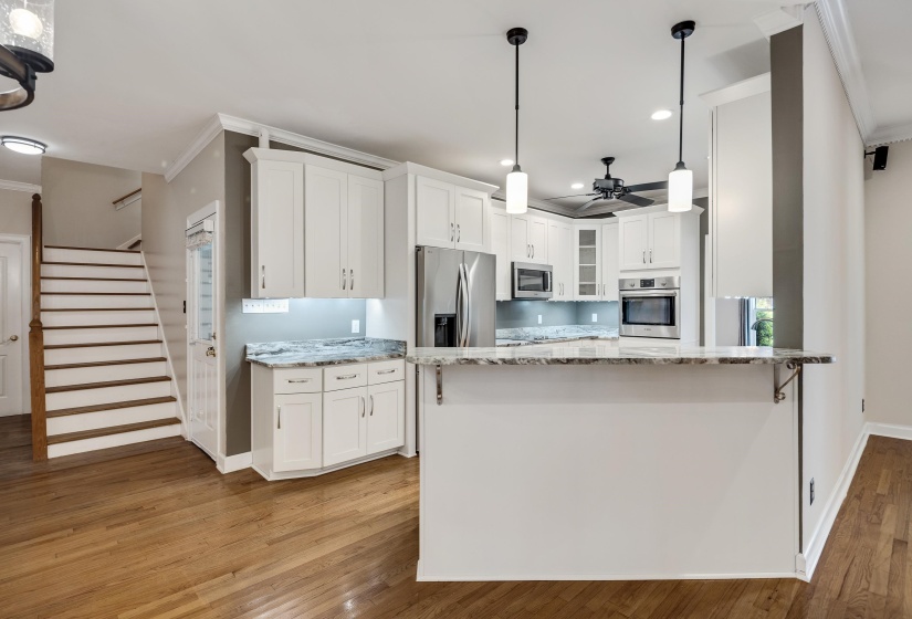 Contemporary kitchen featuring white cabinetry, stainless steel appliances, granite countertops, and a breakfast bar with pendant lighting