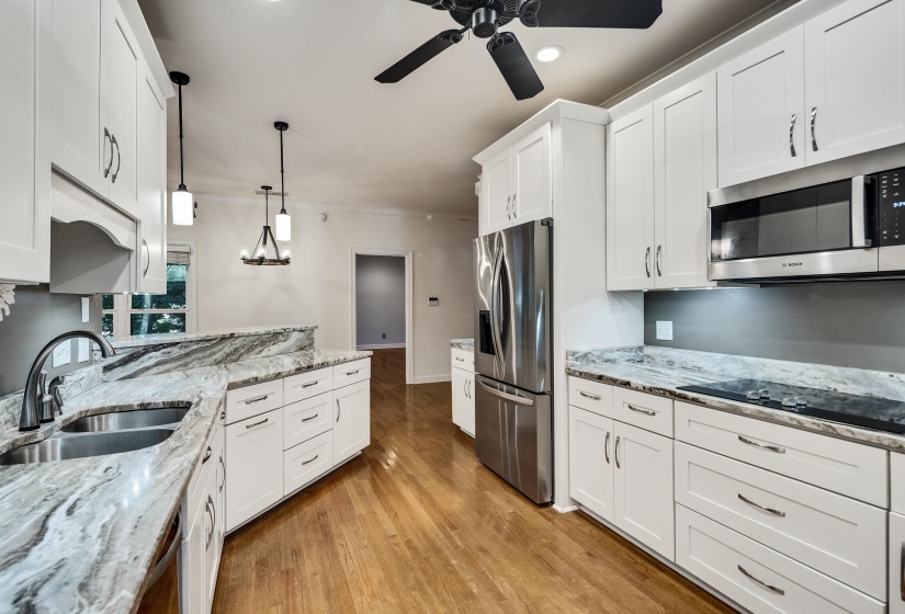 Open-concept kitchen featuring white shaker cabinetry, stainless steel appliances, premium stone countertops, wood-finish flooring, and a double basin sink