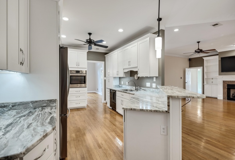 Open-concept kitchen featuring white cabinetry, light-toned countertops, and wood-finish flooring