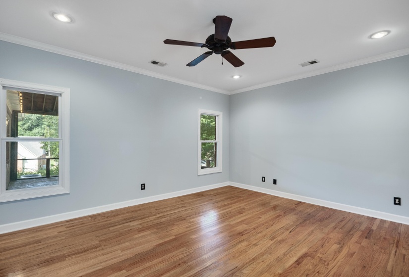Spacious room featuring wood-finish flooring, two windows providing natural light, recessed ceiling lighting, a ceiling fan, and crown molding