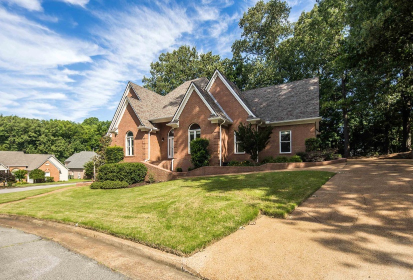 Brick exterior with a gabled roofline, arched windows, and a sloped, landscaped front yard