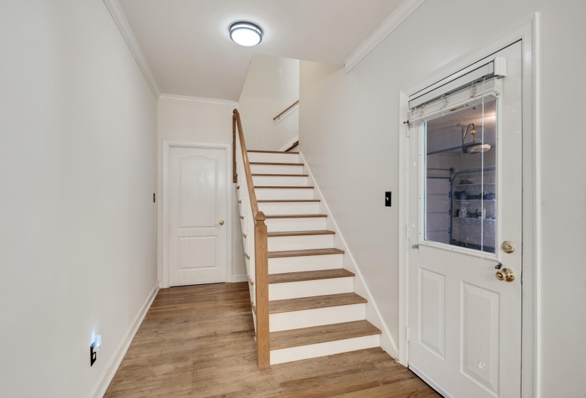 Staircase entryway featuring wood-finish flooring, white risers, and natural wood handrails