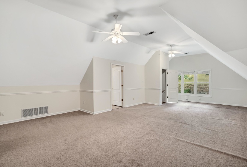 Expansive carpeted room featuring a sloped ceiling design, two ceiling fans with integrated lighting, and white trim molding