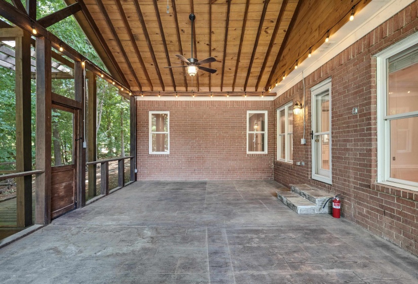 Spacious covered patio featuring a wood-finish ceiling with exposed beams, brick exterior, and a ceiling fan