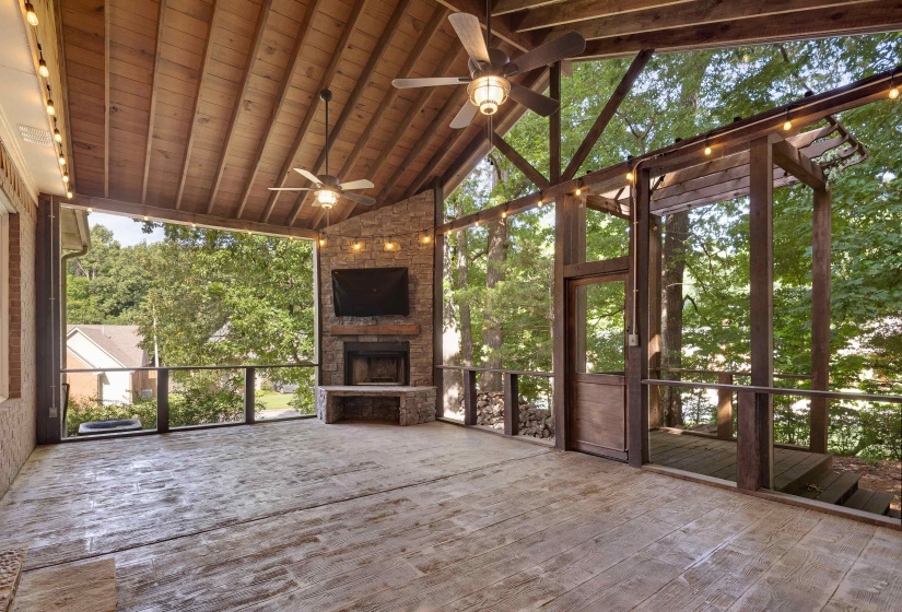 Expansive screened porch featuring a vaulted wood-plank ceiling, wood-finish flooring, a stone-clad fireplace, and dual ceiling fans