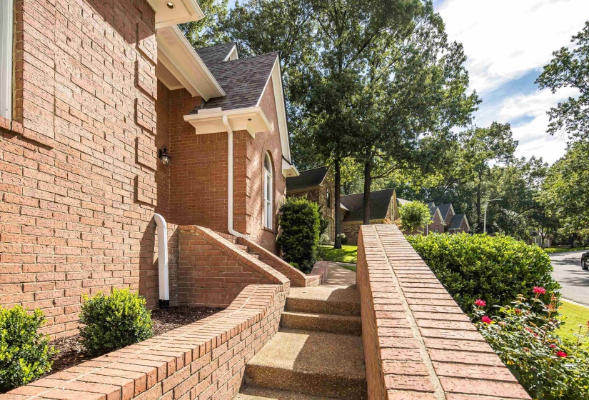 Brick exterior with a gabled roofline, featuring an arched window and a concrete pathway with brick retaining walls