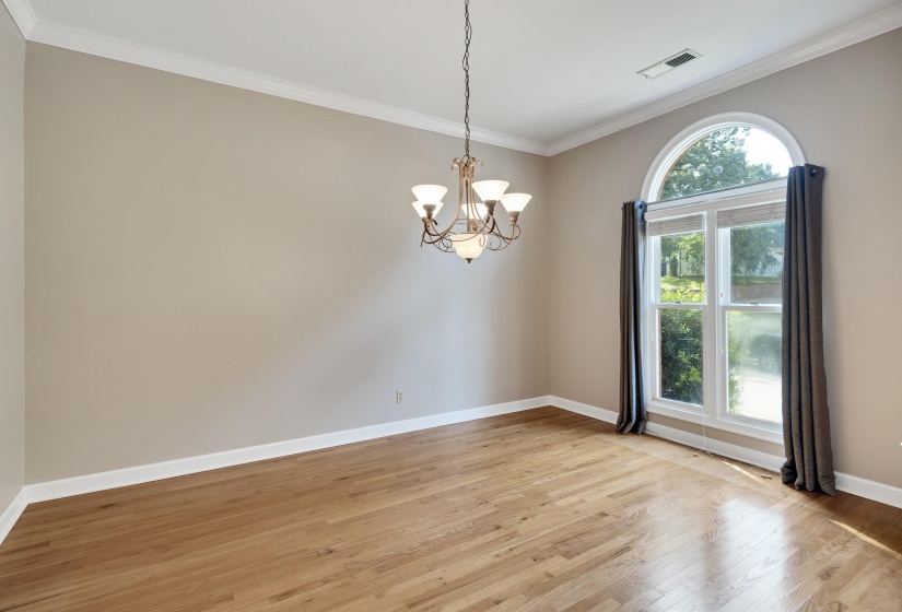 Spacious room featuring wood-finish flooring, crown molding, a five-light chandelier, and an arched window with white trim