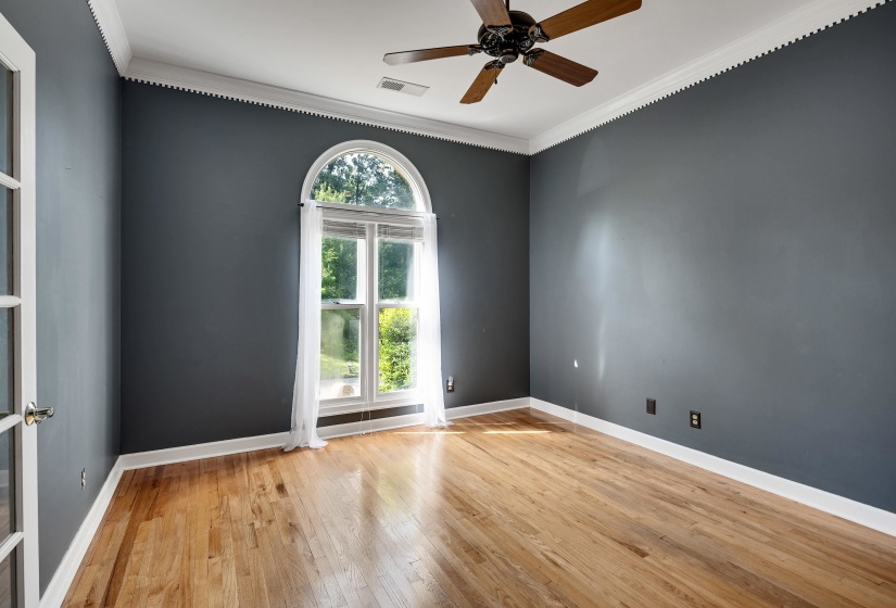Hardwood flooring, arched window with transom, ceiling fan, crown molding, and French doors with privacy glass