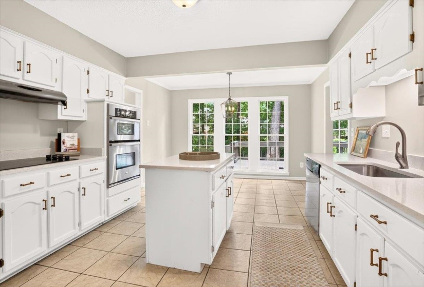 Kitchen featuring white cabinetry, light-toned countertops, stainless steel double wall ovens, a center island, and tile flooring