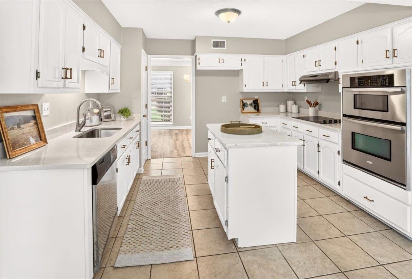 Kitchen featuring white cabinetry with dark bronze hardware, a central island with a solid surface countertop, stainless steel double wall ovens, an integrated cooktop, and tile flooring