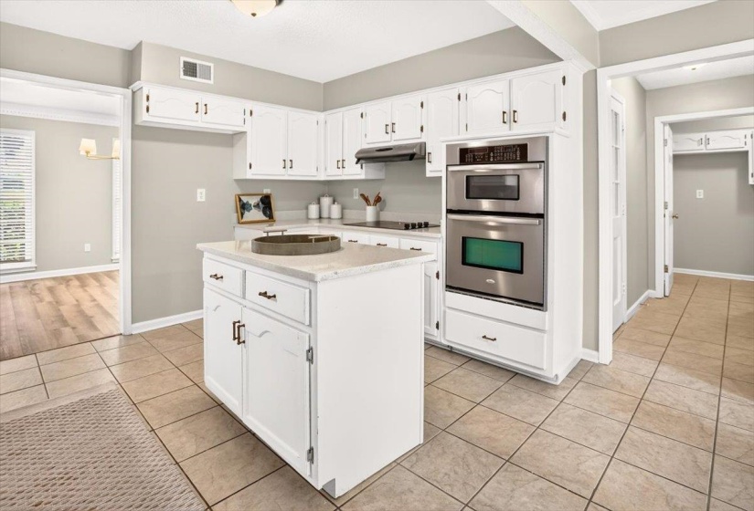 Kitchen featuring white cabinetry, a built-in double oven, stainless steel appliances, a center island with countertop, and tile flooring