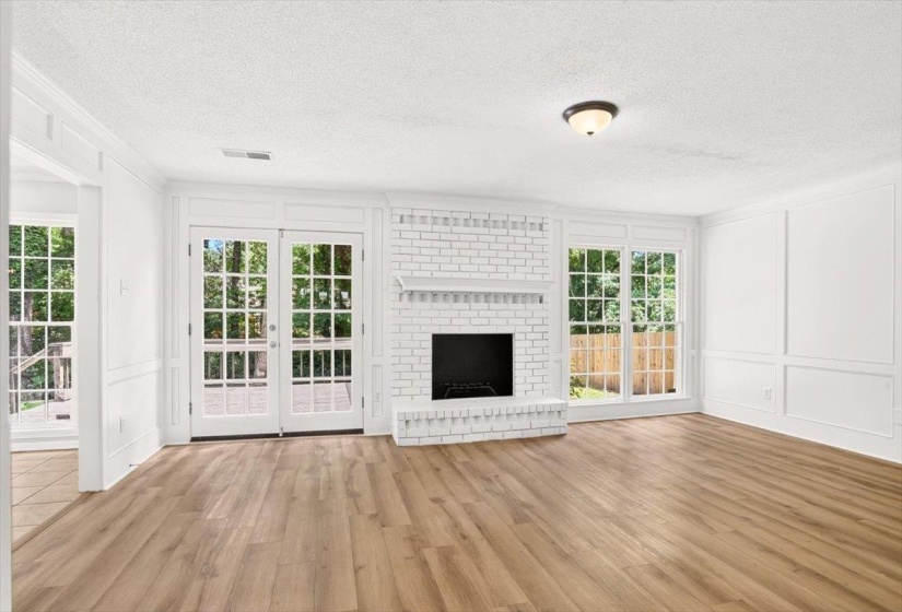 Spacious living area featuring a whitewashed brick fireplace with mantel, French doors, wood-finish flooring, multiple pane windows, and detailed wainscoting