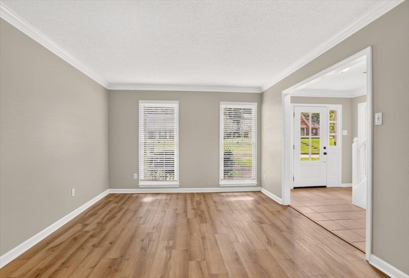 Spacious living area featuring wood-finish flooring, two large windows with blinds, crown molding, and a wide entryway