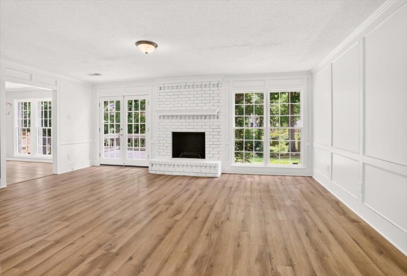 Spacious living area featuring wood-finish flooring, a white brick fireplace with mantel, and ample natural light from multiple large windows