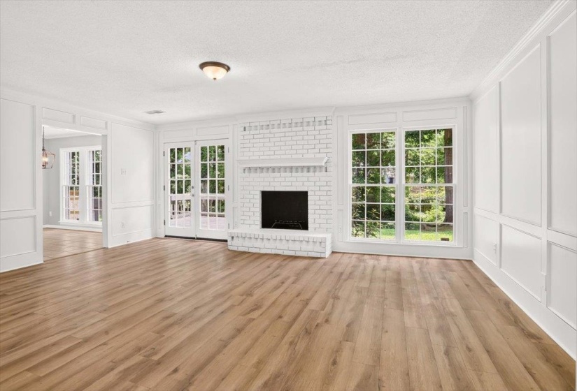 Spacious interior featuring wide plank wood-finish flooring, white brick fireplace, and extensive wainscoting