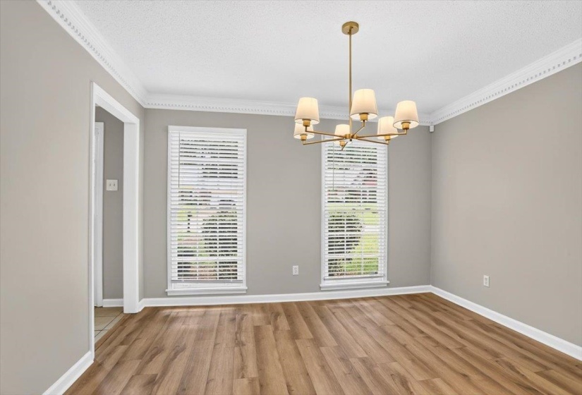 Spacious room featuring wood-finish flooring, neutral-toned walls, and a contemporary brass chandelier