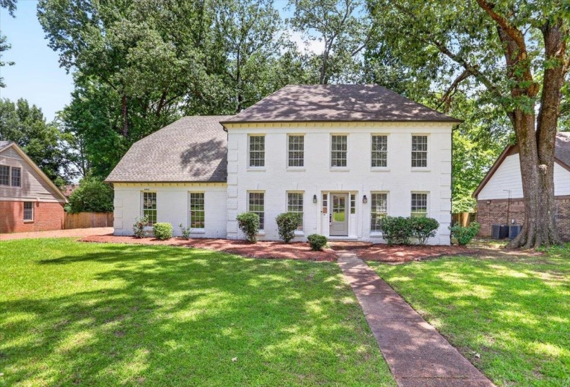 White-painted brick exterior featuring a multi-pane front door with sidelights, decorative shutters, and mature front landscaping