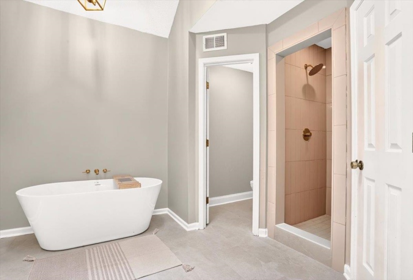 Bathroom featuring a freestanding soaking tub with wall-mounted brass fixtures, a tiled walk-in shower with brass showerhead and controls, and light grey tile flooring