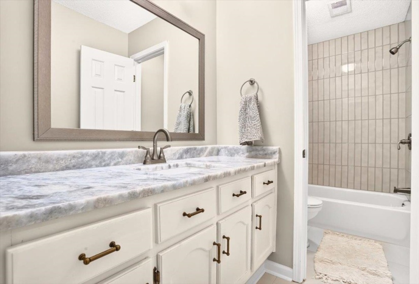 Bathroom vanity featuring a light-toned countertop, dual sinks, and white cabinetry with dark-toned hardware