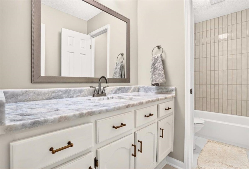 Bathroom vanity featuring a light-colored countertop with integrated sink, white cabinetry with bronze hardware, and an overhead framed mirror