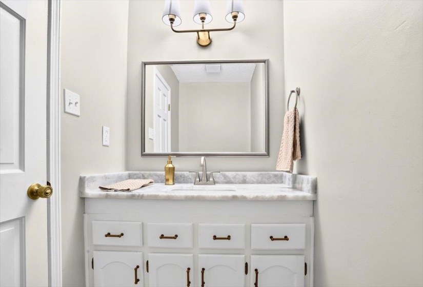 Vanity area featuring a white cabinetry with bronze-tone hardware, a white countertop with integrated sink, and a rectangular framed mirror