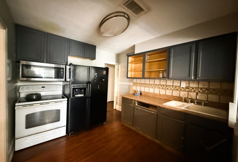 Kitchen featuring white range with electric stovetop, stainless steel microwave, black refrigerator with ice dispenser, light countertops, and open shelves