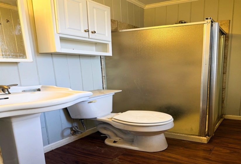 Bathroom with a decorative wall, dark wood finished floors, crown molding, a shower stall, and wood walls