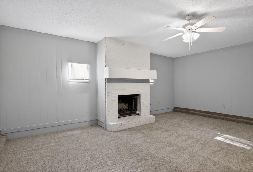 Unfurnished living room featuring light carpet, ceiling fan, a textured ceiling, and a brick fireplace