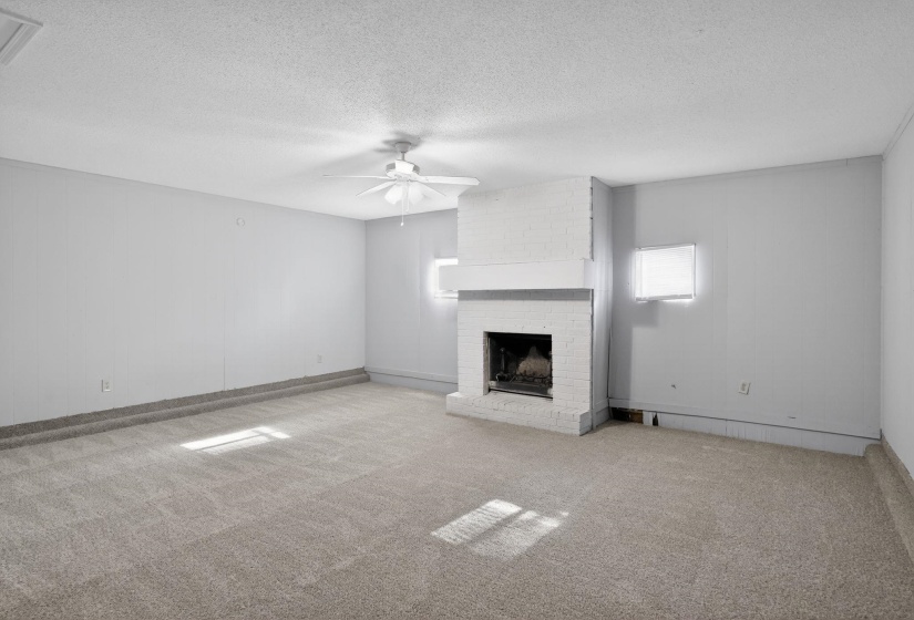 Unfurnished living room with light colored carpet, a textured ceiling, a ceiling fan, and a brick fireplace