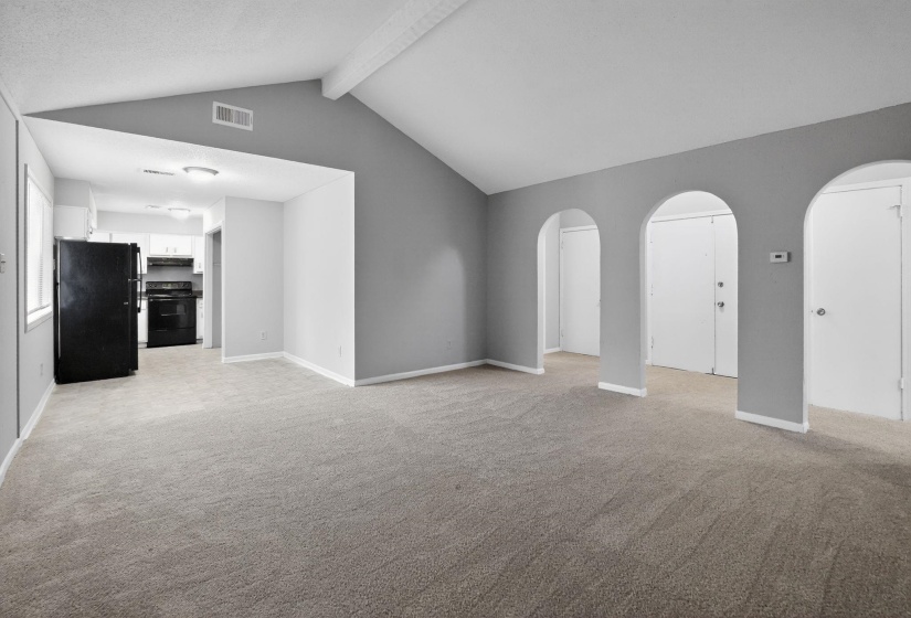 Unfurnished living room with arched walkways, light colored carpet, and beamed ceiling
