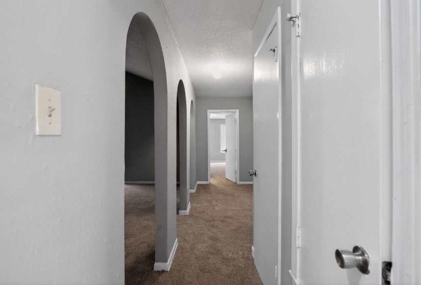 Corridor with arched walkways, light carpet, and a textured ceiling