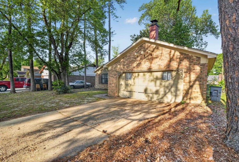 View of property exterior with brick siding, a chimney, driveway, and a garage