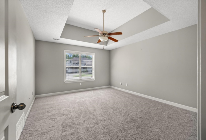 Spacious room featuring a tray ceiling with a ceiling fan, neutral wall paint, and plush carpeting
