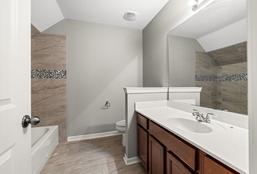 Full bathroom featuring a single vanity with wood-finish cabinetry, a white countertop, and an integrated basin