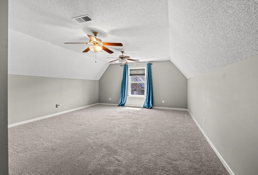 Spacious room with sloped ceilings, two ceiling fans, light gray wall paint, and gray carpeting
