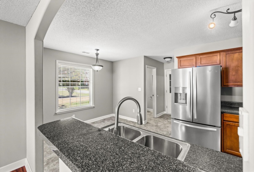 Kitchen featuring a double basin stainless steel sink, dark speckled countertop, stainless steel refrigerator, and wood cabinetry