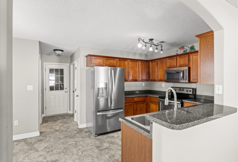 Kitchen featuring wood cabinetry, stainless steel appliances, dark stone-finish countertops, and a double-basin stainless steel sink with a high-arc faucet