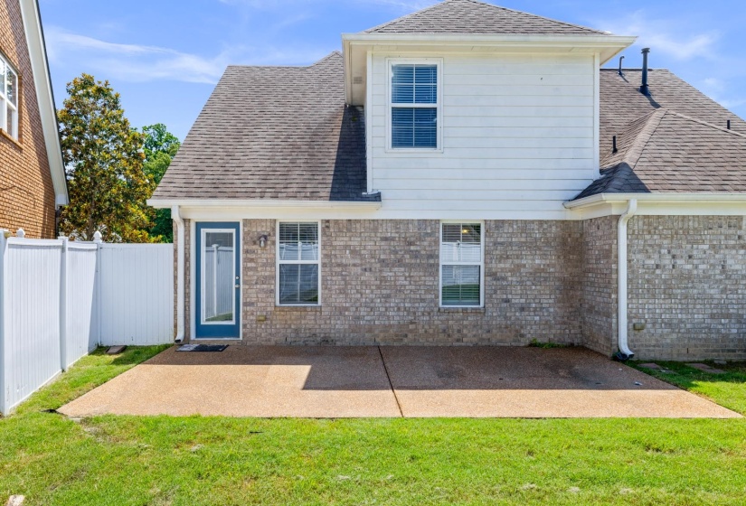 Rear exterior featuring a spacious concrete patio, brick and white siding facade, a blue-framed glass panel door, and a white privacy fence