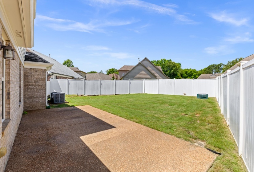 Expansive backyard featuring a concrete patio, a manicured lawn, and a white privacy fence