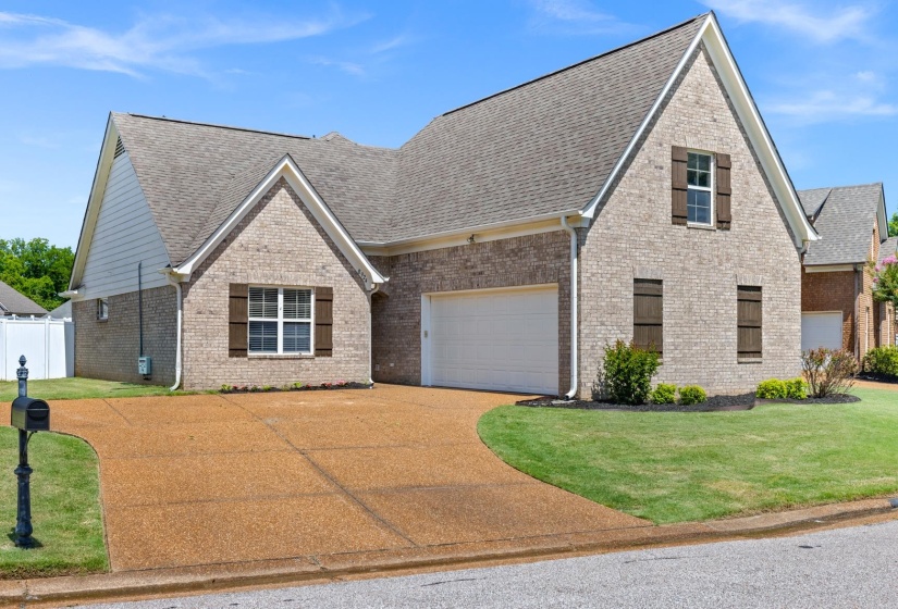 Brick facade residence featuring a two-car garage, pitched roofline, and decorative window shutters